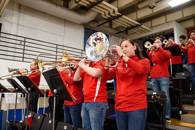 Mellophone player with shiny silver bell next to trombones at basketball game