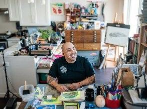 哈维尔·弗洛雷斯在他的家庭艺术工作室里，周围都是版画材料. 他微笑着，抬头看着他的右边