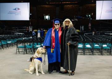 在2023年5月的毕业典礼上，道恩·布克哈特与一名视障学生和他的狗站在一起